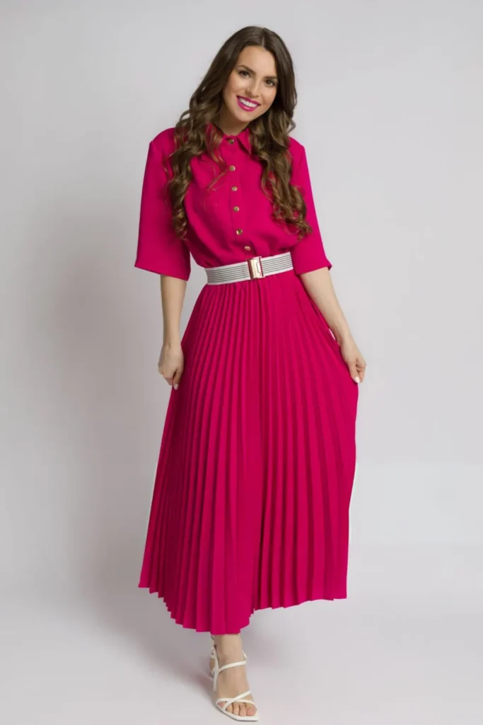 Smiling woman in a vibrant magenta pleated midi dress with a waist-defining belt and white sandals.