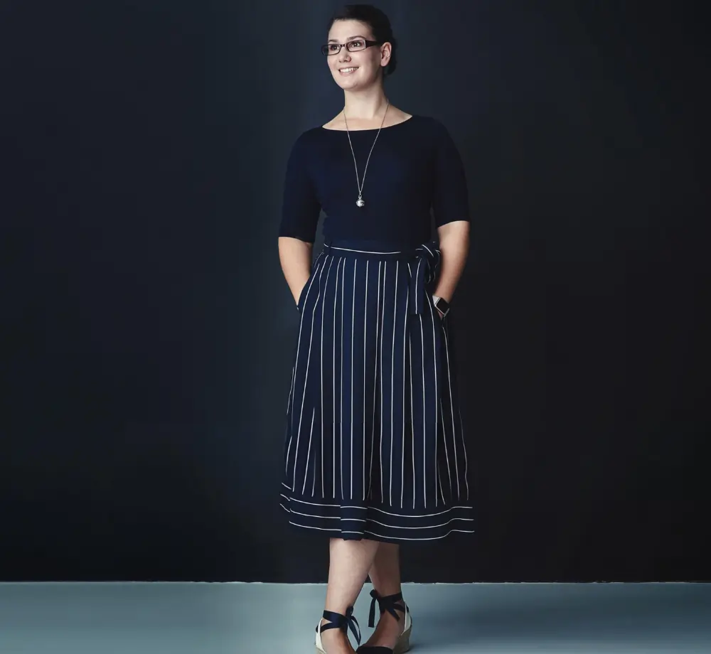 Smiling female healthcare professional in professional navy attire with striped skirt and glasses.