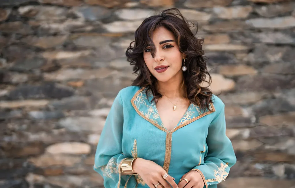 Smiling woman in a turquoise kaftan with gold embroidery, promoting cultural wellness and confidence.