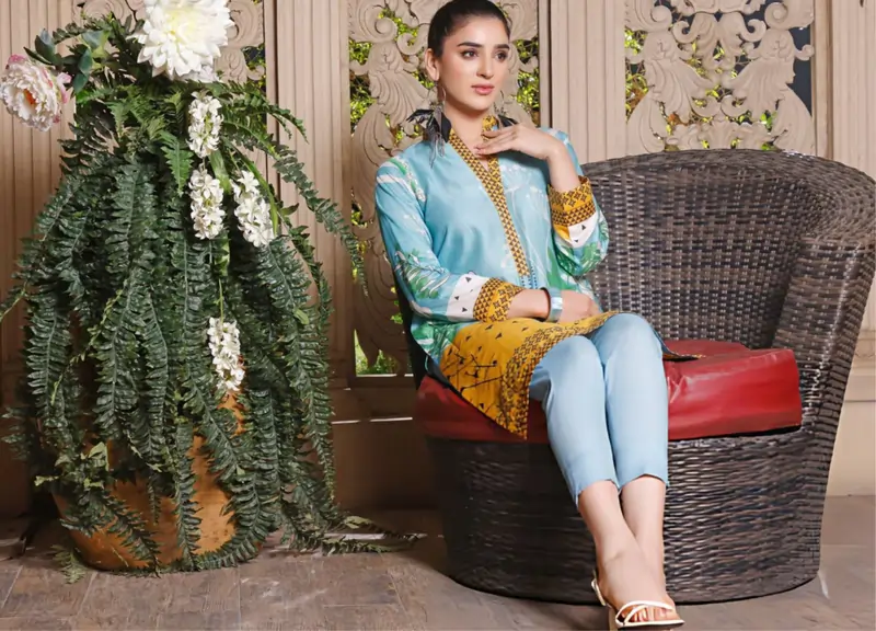 Woman in a blue and yellow printed tunic and trousers, sitting comfortably in a woven chair.