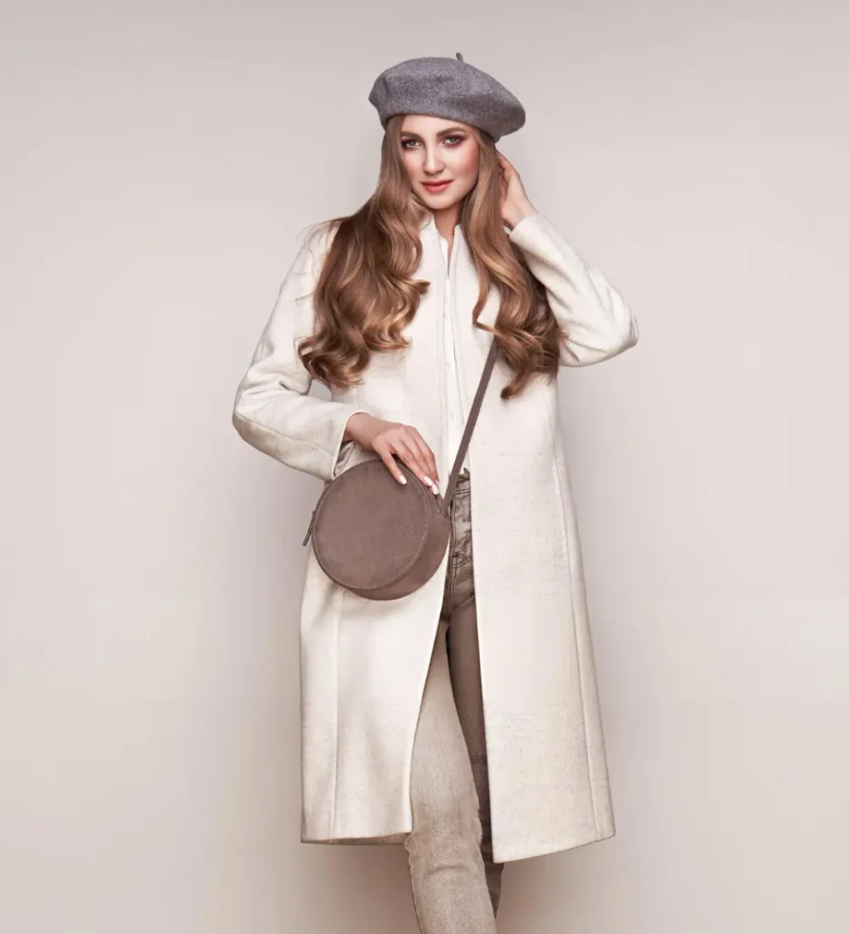 Woman in cream coat and grey beret posing for a seasonal wellness and fashion editorial.