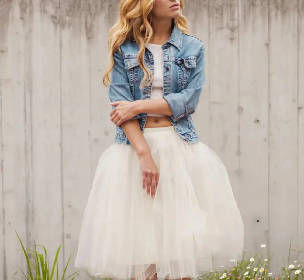 Woman in denim jacket and white tulle skirt posing outdoors, promoting youthful vitality.