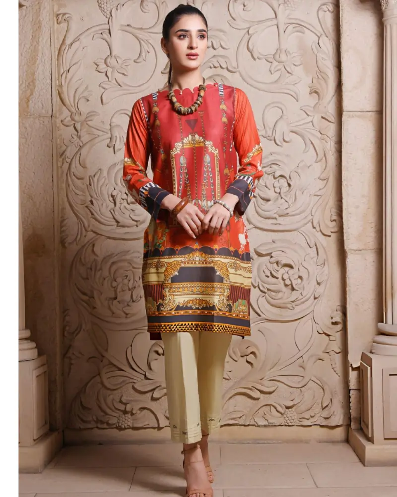 Woman in orange printed kurta and beige trousers posing against a carved wall for a wellness shoot.